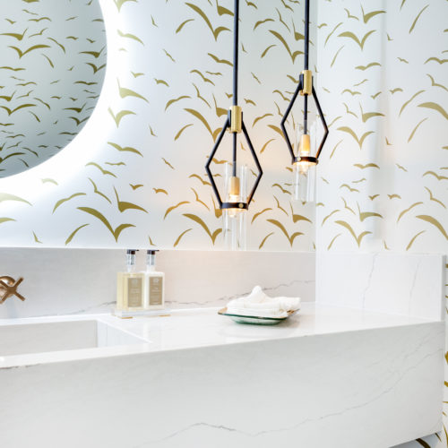 Luxurious bathroom with printed wallpaper, circular mirror, and elegant pendant lighting.