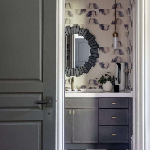 A bathroom with a stunning mirror framed by wallpaper and illuminated by a pendant light.