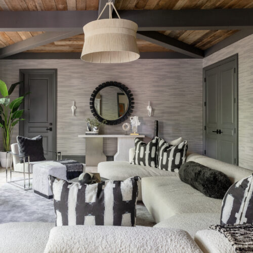 A living area with an artistic touch, featuring a bold art piece, pendant light, black and white printed pillows, and a round mirror above a console table.